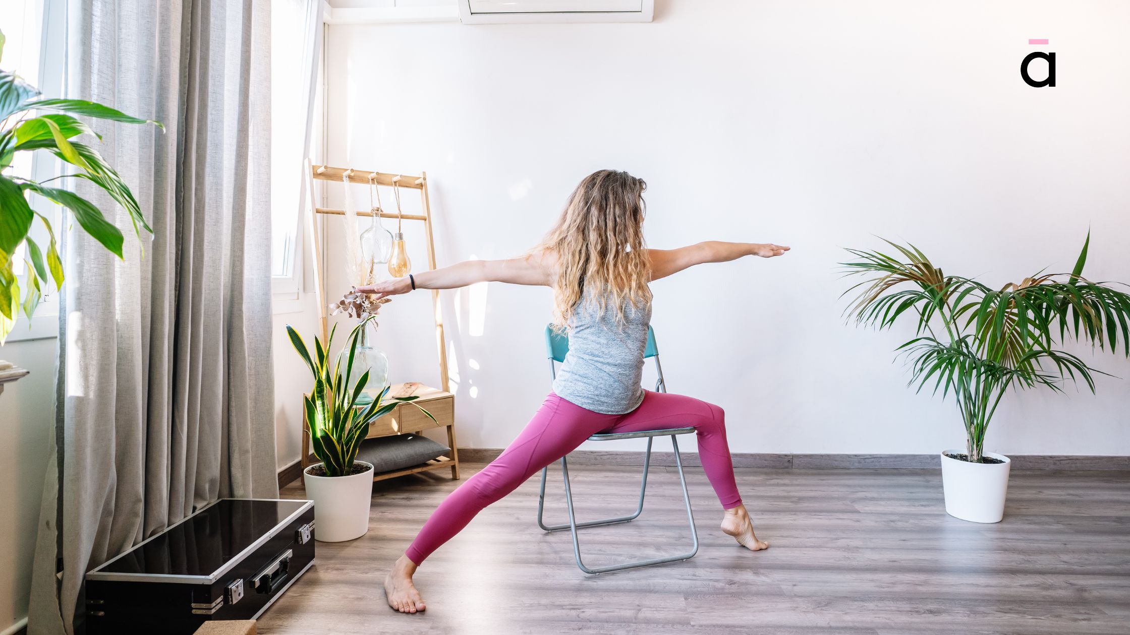 Woman practising Virabhadrasana II seated on a chair, focusing on strength and grounding in a home yoga studio